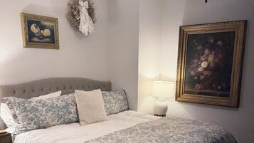 Une chambre à coucher avec un lit, une table de chevet, des œuvres d’art murales et un ventilateur de plafond.