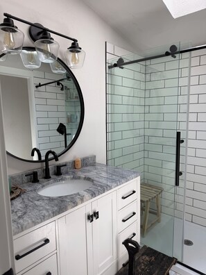 Un baño con lavamanos blanco, grifo negro y cabina de ducha de vidrio.