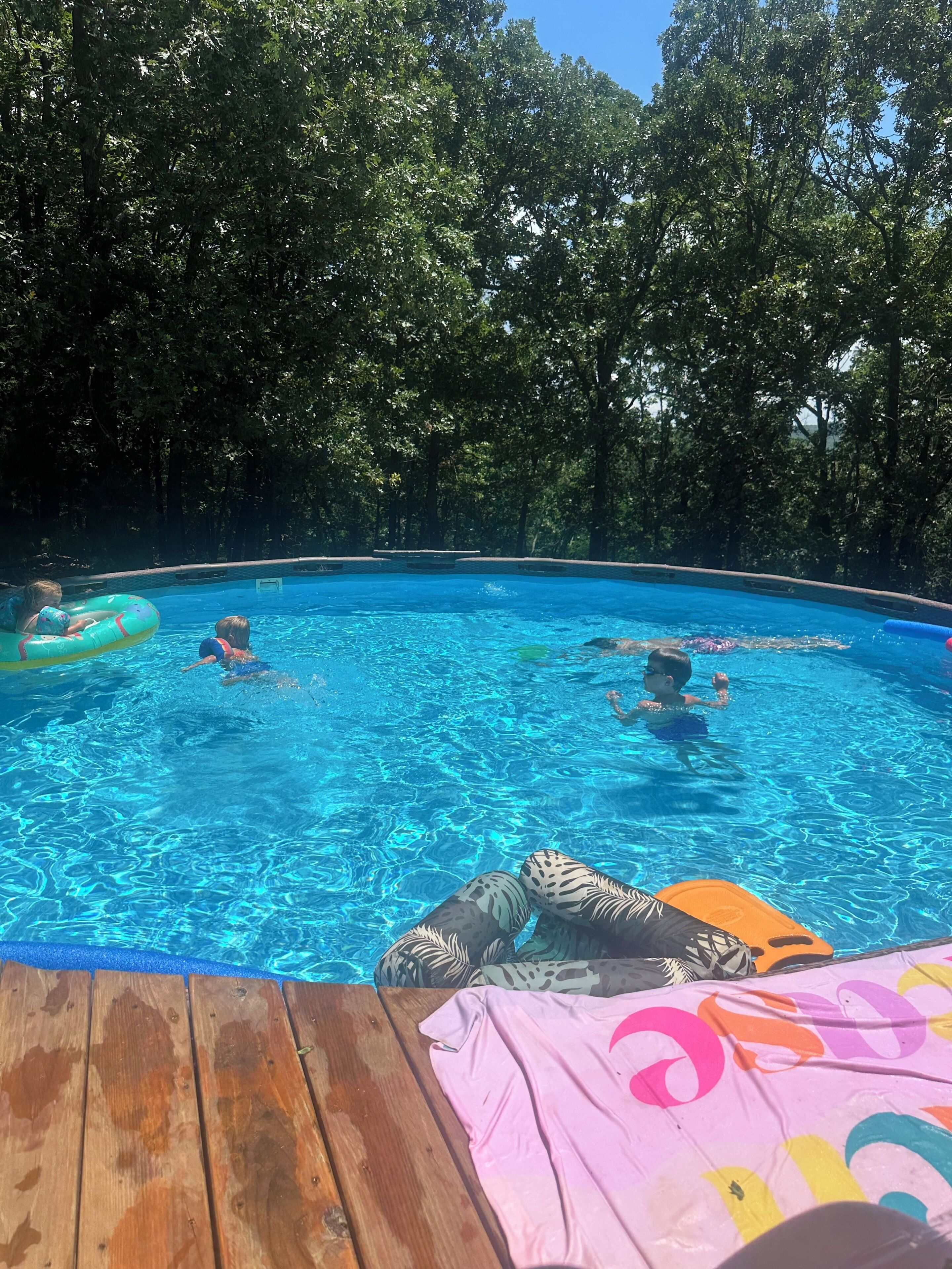 Una piscina rodeada de árboles, con una terraza de madera al frente.