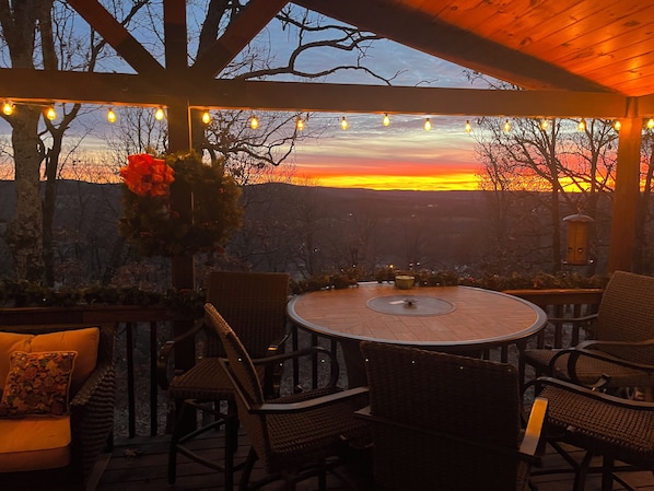 An outdoor patio with wicker furniture, a round table, and a view of a sunset.