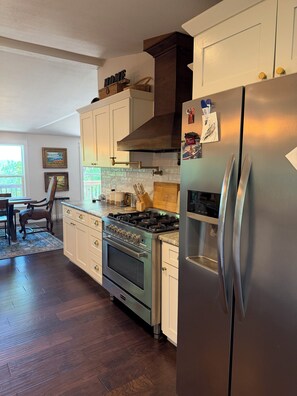 A kitchen with a stainless steel refrigerator, a stove, and white cabinetry.