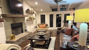 Una sala de estar con chimenea, televisor, ventilador de techo y un sofá.