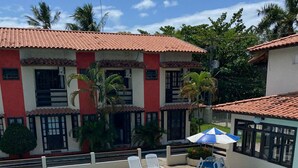 A swimming pool with lounge chairs and an umbrella, surrounded by buildings with red-tiled roofs and palm trees. - Nazareth Residential, apartment 16 (Porto Seguro)