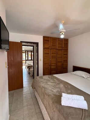 A bedroom with a bed, a wooden wardrobe, a ceiling fan, and a television. - Nazareth Residential, apartment 16 (Porto Seguro)