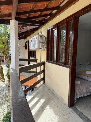 A balcony with a wooden railing, a bed with a white bedspread, and an air conditioning unit mounted on the wall. - Nazareth Residential, apartment 16 (Porto Seguro)