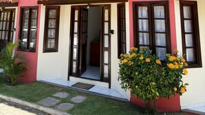 A two-story building with a red and white facade, balconies, and a small garden with yellow flowers. - Nazareth Residential, apartment 16 (Porto Seguro)