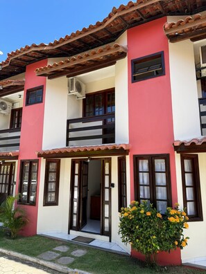 A two-story building with a red and white facade, balconies, and a small garden with yellow flowers. - Nazareth Residential, apartment 16 (Porto Seguro)