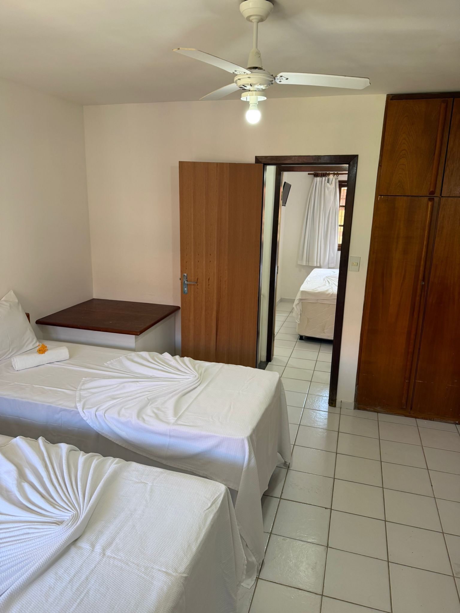 Una habitación de hotel con dos camas, un ventilador de techo, un armario de madera y una mesita pequeña.