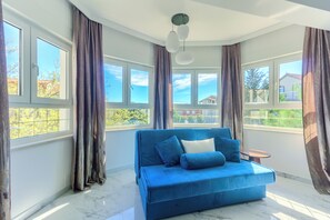 A room with a blue sofa, large windows, and a view of buildings outside. - Magical Villa ,between old town; Split - Trogir , with heated pool and jacuzzi. (Kaštel Štafilić)