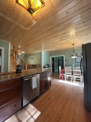A spacious kitchen with wooden flooring, a granite countertop, and a stainless steel refrigerator.