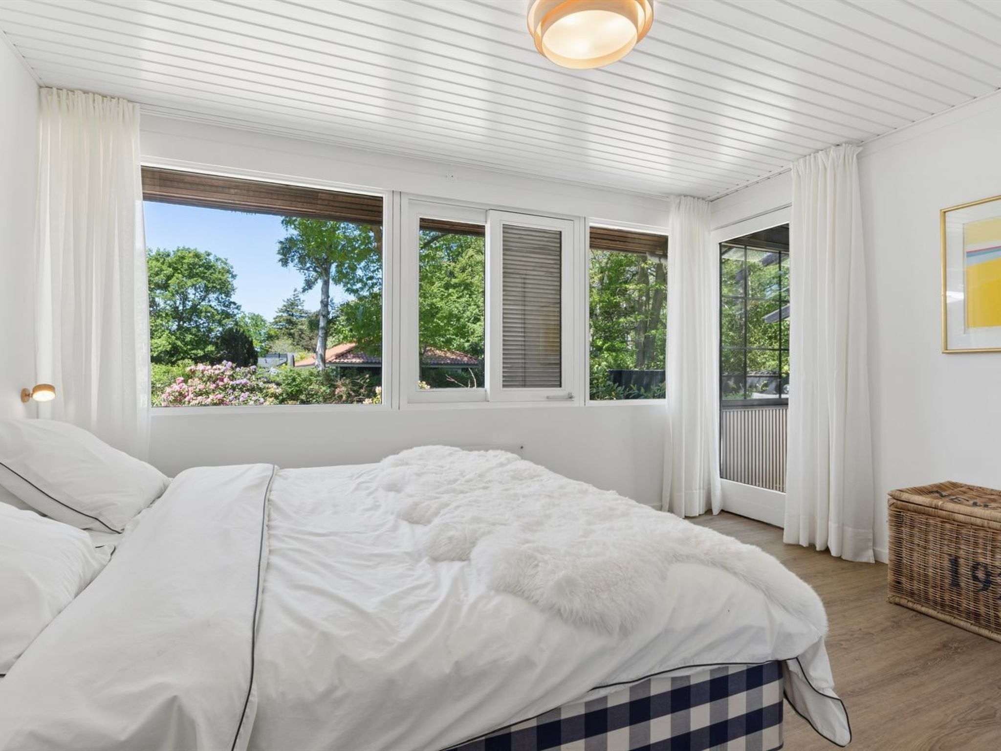 Un dormitorio con una cama grande, cortinas blancas y vistas a la vegetación.