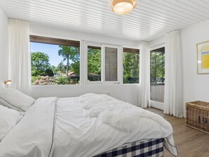 Ein Schlafzimmer mit einem großen Bett, weißen Vorhängen und Blick auf Grün.