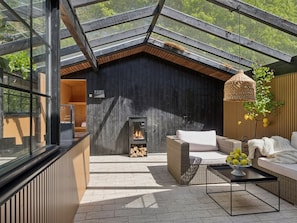 Ein moderner Außenbereich mit Glasdach, Kamin, Korbmöbeln und einer Holzwand.