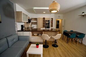 A modern kitchen with wooden cabinets, a white countertop, and a dining area with a table and chairs. - Nikolai Suite (Hamburg)