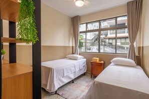 A room with two beds, a window with a view, a wooden desk, and a hanging plant. - Shopping at your doorstep | 3-Bedroom Apartment in Barra (Salvador)