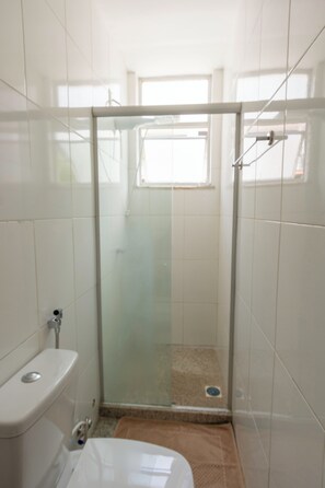 Ein kleiner, abgeschlossener Duschbereich mit Glastür, Toilette und Fenster.