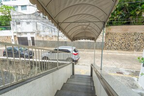 Eine Treppe führt zu einem überdachten Bereich, mit einem geparkten Auto und einer Steinmauer im Hintergrund.