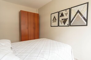 Ein Schlafzimmer mit einem Bett, einem Kleiderschrank und drei gerahmten geometrischen Kunstwerken an der Wand.