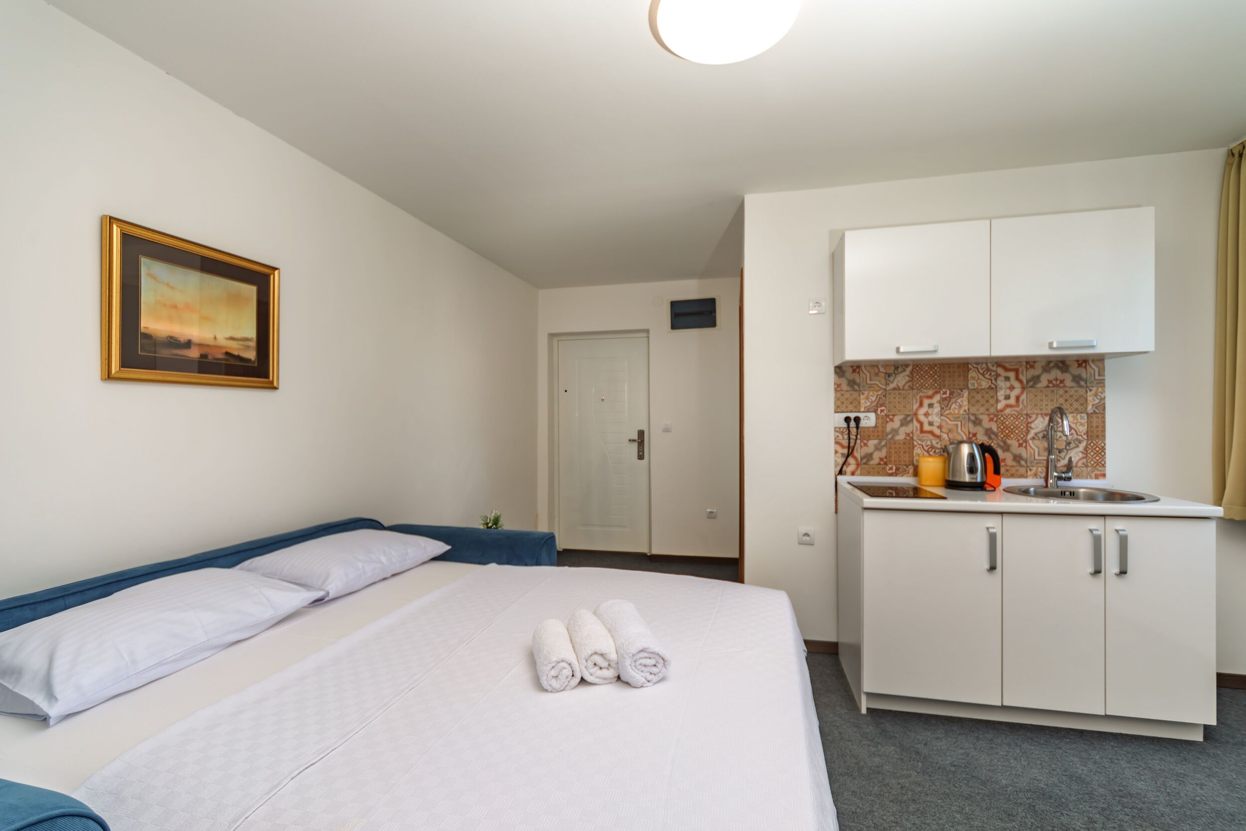 Une chambre d’hôtel avec un lit, un tableau encadré, une kitchenette et une porte.