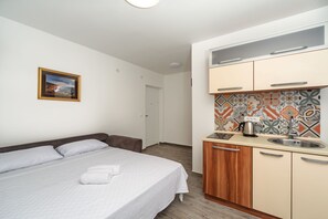 Hotellihuone, jossa on sänky, pieni keittokomero, kylpyhuone ja seinällä oleva kehystetty kuva.
