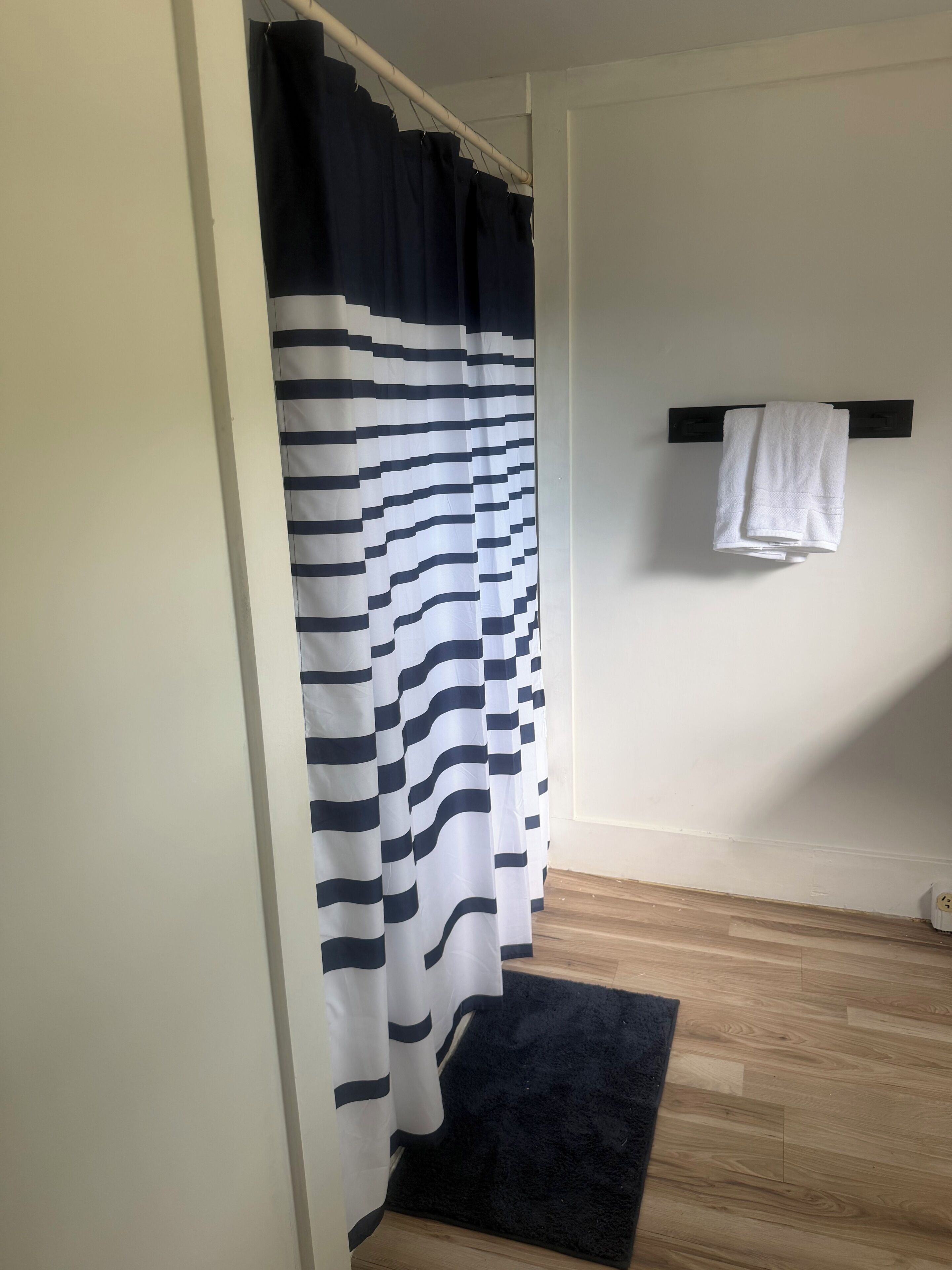 A bathroom with a striped shower curtain, a black towel rack with a white towel, and a wooden floor.