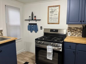 A kitchen with a stainless steel stove, a wooden countertop, and a wall-mounted shelf with kitchen items. - Charming 3-bedroom apartment with AC in Naples (Naples)