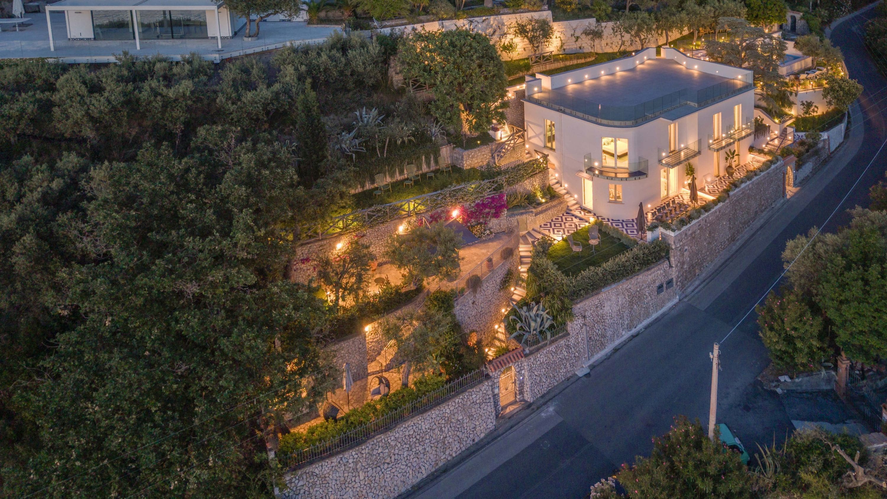 Uma casa moderna com um muro de pedra, um pátio pavimentado e um jardim bem iluminado.