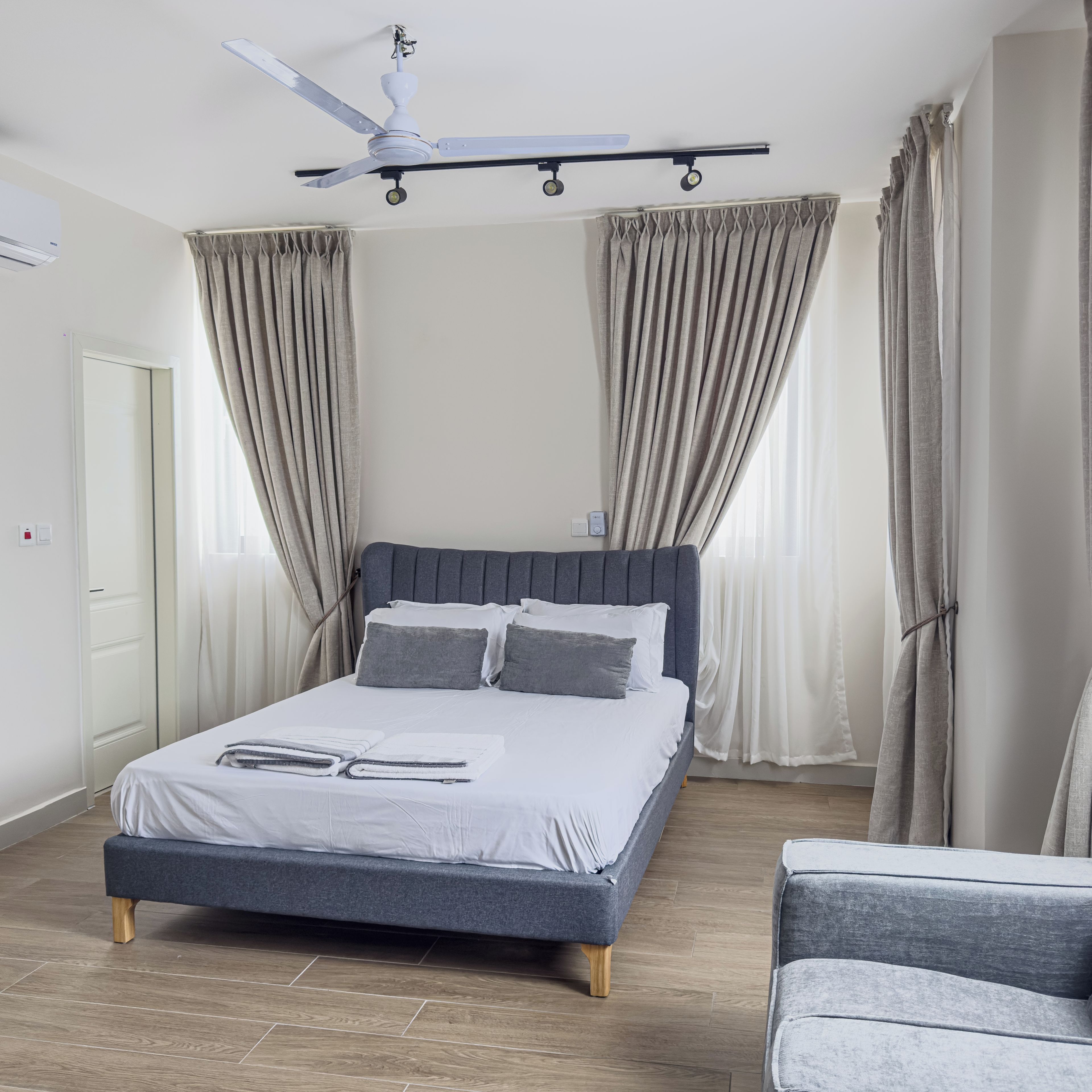 Quarto moderno com cama, cadeira, ventoinha no teto e cortinas.