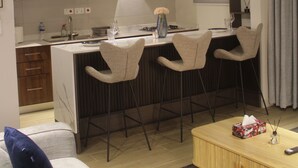 A modern kitchen with a central island, bar stools, a ceiling fan, and a dining area with a sofa and coffee table. - Peaceful 3-bedroom building with AC in vibrant Accra (Accra)
