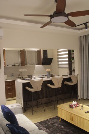 Eine moderne Küche mit einer zentralen Kochinsel, Barhocker, Deckenventilator und einem Essbereich mit Sofa und Couchtisch.