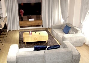 Ein modernes Wohnzimmer mit Flachbildfernseher, grauen Sofas, einem Holztisch und einer Bar mit Hockern.