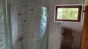 A shower with a glass door, a window with a view of greenery, and tiled walls. - Mirage House in Karhumäki (Etelä-Karjala)