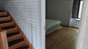 Eine Treppe mit Holzhinweisen und schwarzen Wangen, ein Bett mit weißer Matratze und grüner Bettwäsche sowie ein Fenster mit Jalousien.