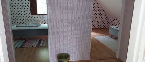 Un dormitorio con cama, ventana, pared estampada, cesto de basura y suelo de madera.