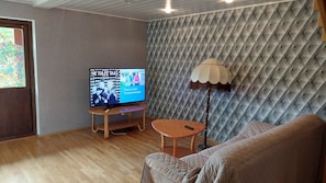 Une pièce comprenant un téléviseur posé sur un meuble, une table ronde, une lampe et un canapé.