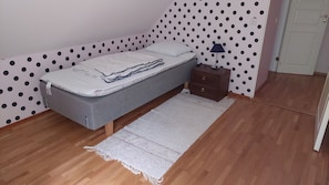 Une petite pièce avec un lit, une table de chevet, une lampe et un mur à motifs à pois.