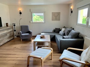 A modern living room with a grey sofa, a wooden coffee table, a grey armchair, and a white bench. - Idyllic vacation home in a quiet location (Höhenland)