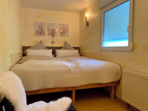 A bedroom with a bed, pillows, a wall-mounted light, and a window with blinds. - Idyllic vacation home in a quiet location (Höhenland)