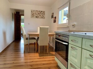 A kitchen with a wooden floor, a dining table with chairs, a built-in oven, and a window. - Idyllic vacation home in a quiet location (Höhenland)
