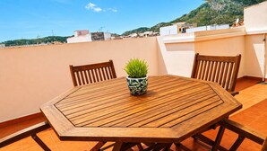 A wooden table with chairs and a potted plant on a rooftop terrace with a view of buildings and hills. - Large Duplex Penthouse with terrace, AC, Wifi and very spacious beds (Orpesa)