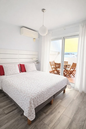 Ein Schlafzimmer mit Bett, Deckenventilator, Fenster und Blick ins Freie.