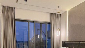 Habitació d'hotel moderna amb un llit gran, vista a la ciutat i un balcó amb una cadira penjant.