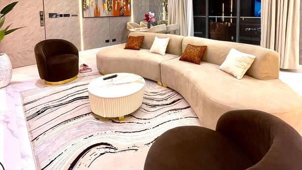 Un saló modern amb un sofà modular, un otoman rodó, un butac armchair i una finestra gran amb cortines.