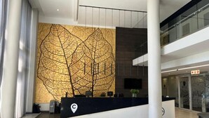 Een moderne hotellobby met een receptiebalie, een grote abstracte wanddecoratie en een trap naar een hoger niveau.