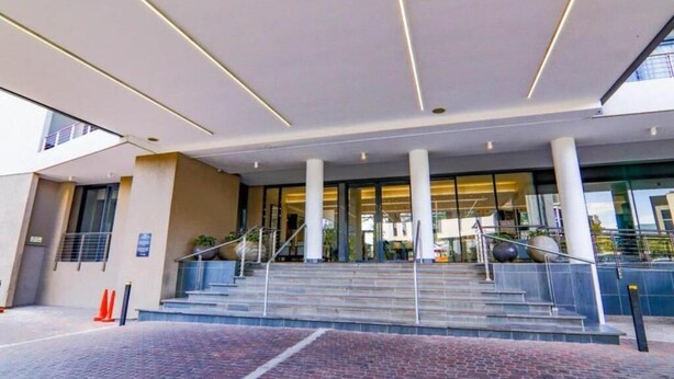 Een moderne hotelingang met een glazen gevel, een trap die naar de lobby leidt, en een grindpad.