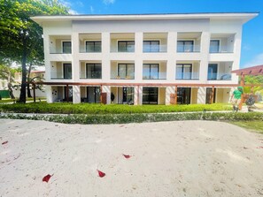 Un hotel de varios pisos con balcones, un paseo techado y un jardín bien cuidado.