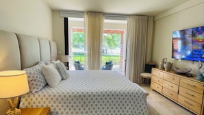 Hotellihuone, jossa on sänky, televisio, puinen lipasto ja näkymä ulos.