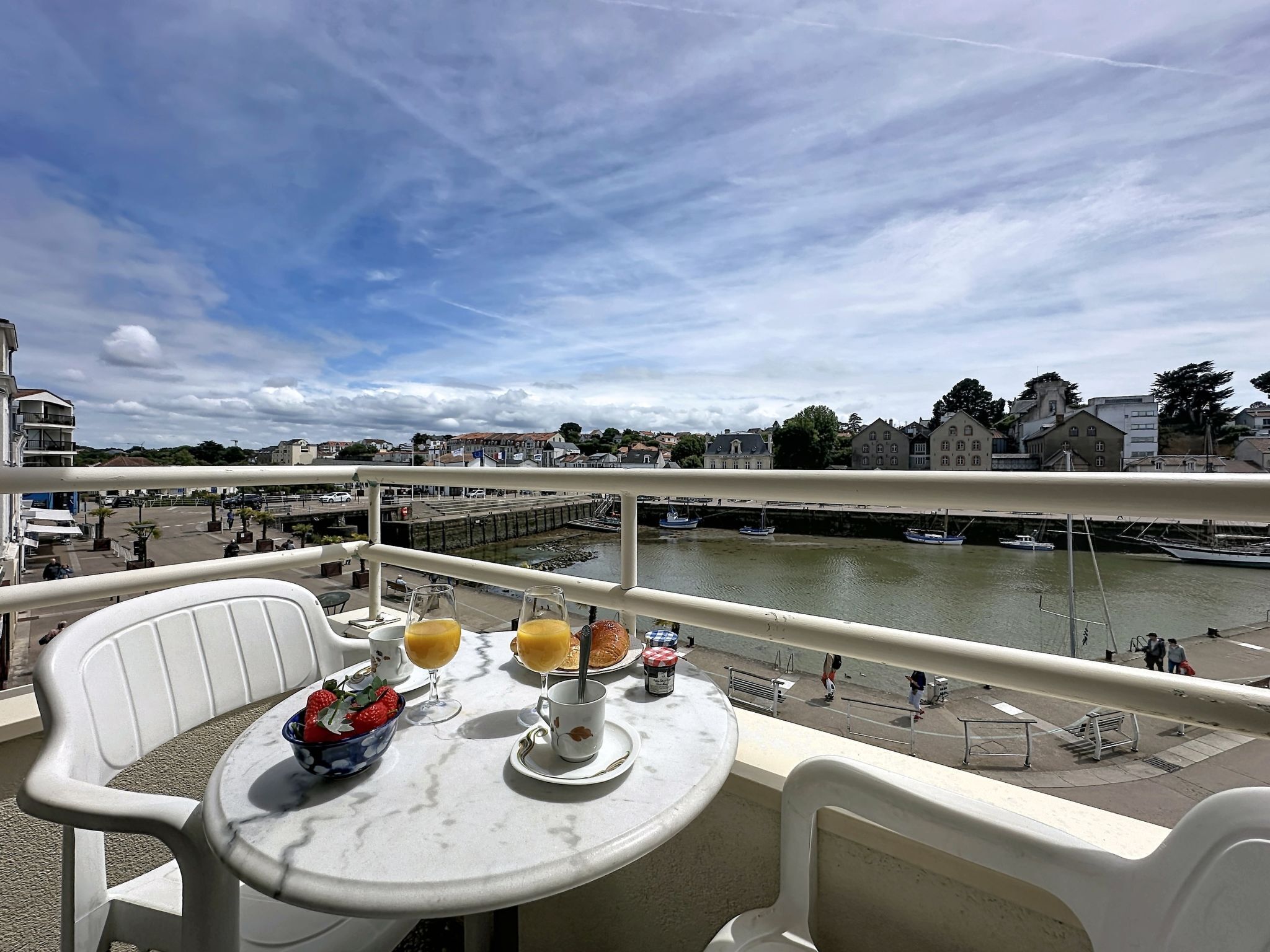 A balcony with a table set for breakfast, overlooking a river with boats and buildings.