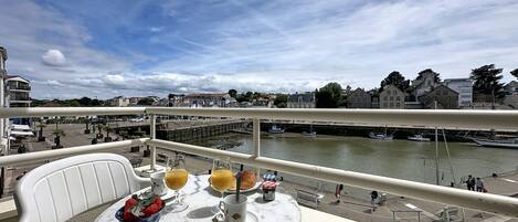 A balcony with a table set for breakfast, overlooking a river with boats and buildings.
