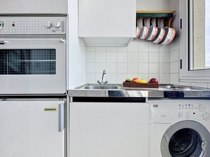 Ett kompakt kök med en inbyggd ugn, en tvättmaskin, ett handfat och en torkställning.